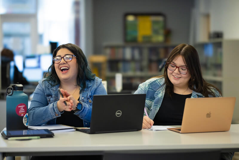 Two students laugh while studying together in the library.